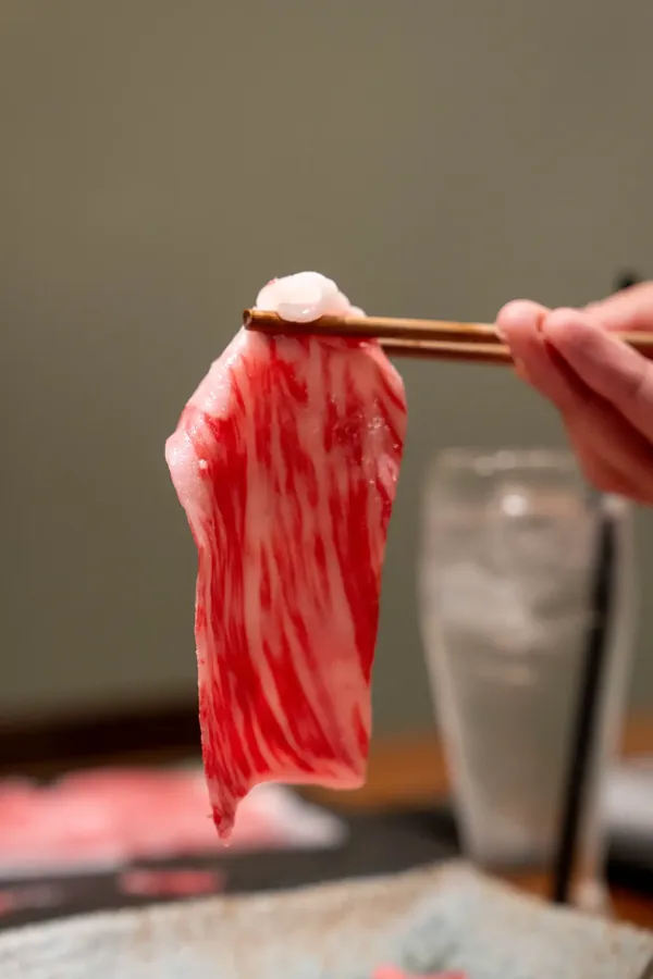 A single slice of marbled Kuroge Wagyu held up with chopsticks
