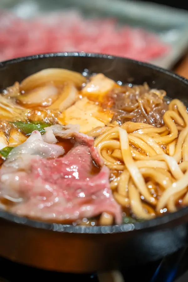 Raw marbled Wagyu laid over the simmering sukiyaki pot
